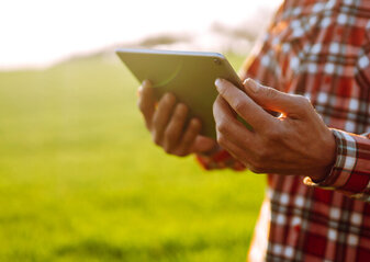 Na zdjęciu widać osobę na polu, trzymającą i spoglądającą na tableta.