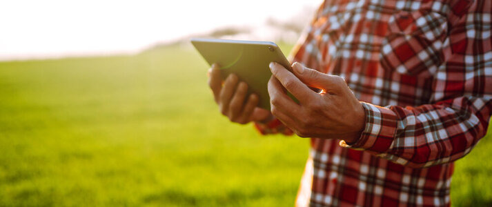 Na zdjęciu widać osobę na polu, trzymającą i spoglądającą na tableta.