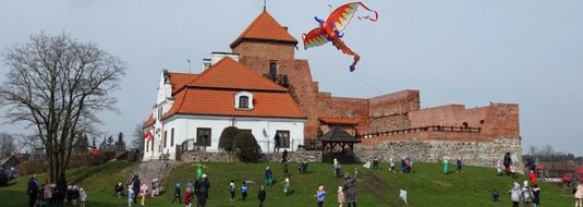 Widok na Zamek w Liwie. Na podzamczu dzieci puszczające latawiec - zielony smok na podzamczu